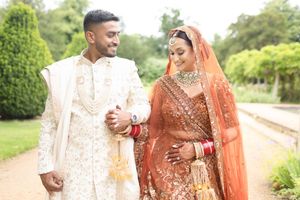 Indian bride and groom in traditional wedding attire walking together in a lush garden setting.