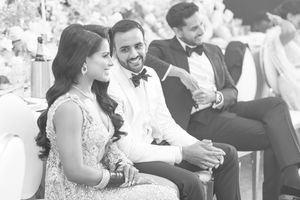 Black and white photo of a smiling couple in formal attire seated at an elegant wedding reception.