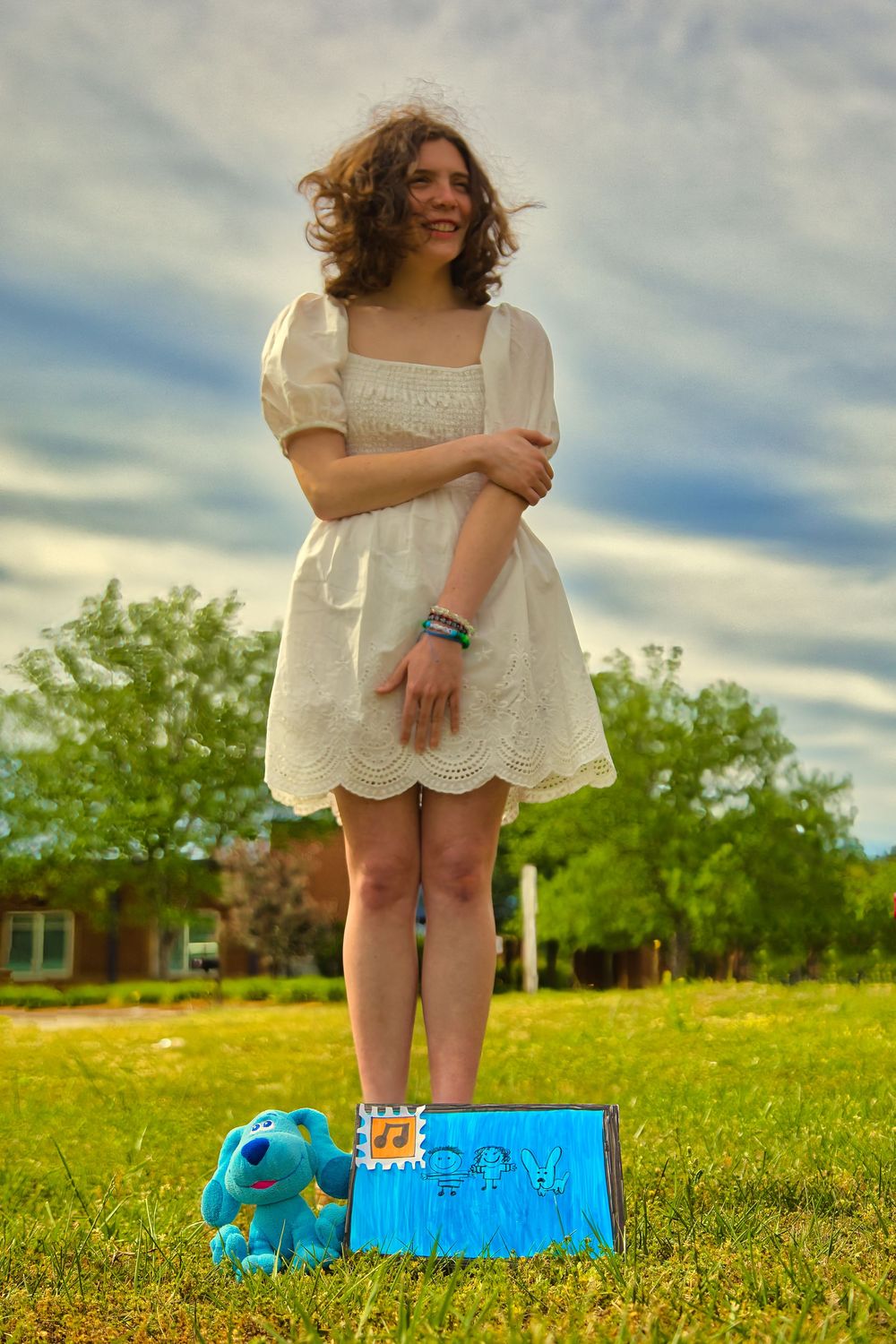 Young woman in white dress standing on grass with Blue's Clues stuffed animal and blue box.