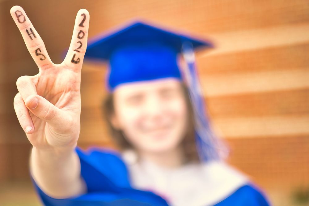 Graduate in blue cap and gown showing peace sign with BHS 2025 written on fingers.