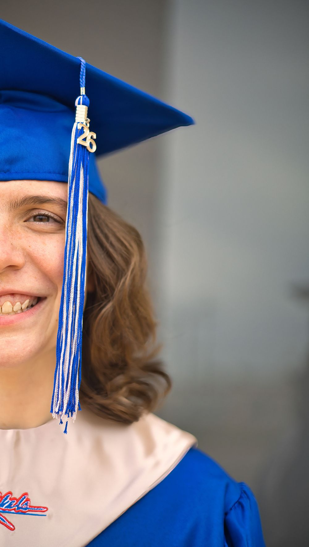 Smiling female graduate in blue cap and gown with 2026 tassel closeup portrait.