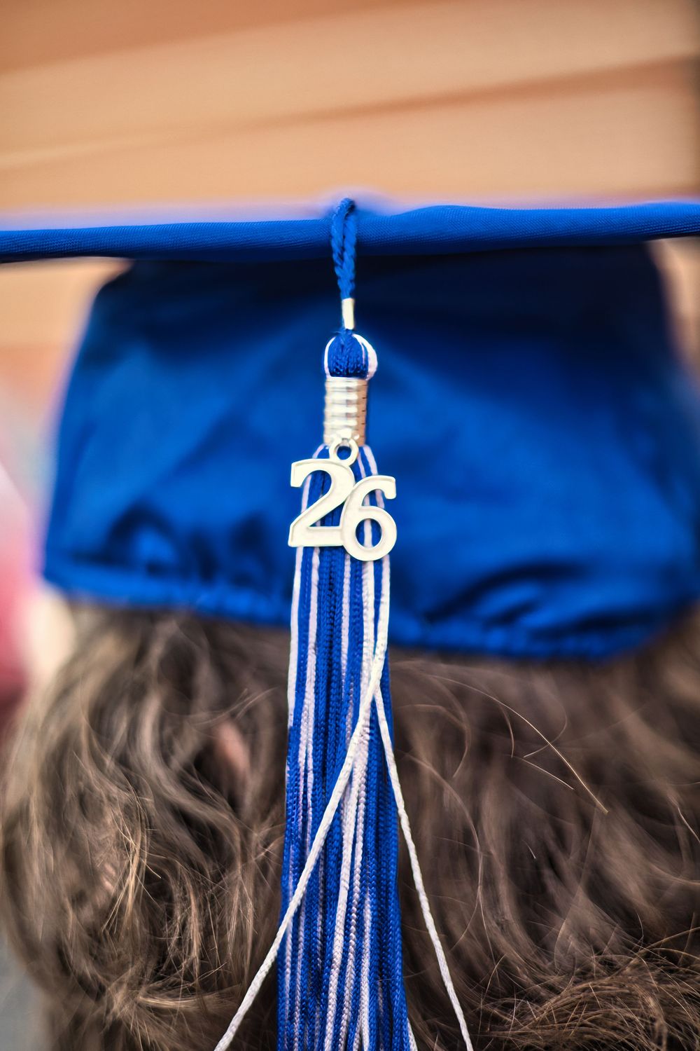 Close-up of blue graduation cap with gold 2026 tassel charm on curly hair.