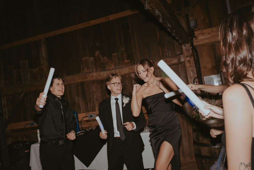 Guests dancing with glow sticks at a rustic barn wedding reception in formal attire.