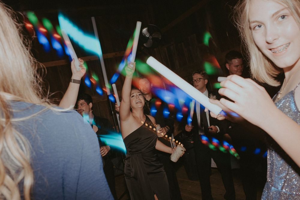People dancing at a party with colorful LED glow sticks under festive lighting.