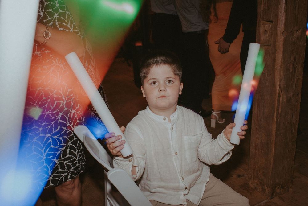 Young boy in white shirt holding colorful LED glow sticks at a wedding reception party.