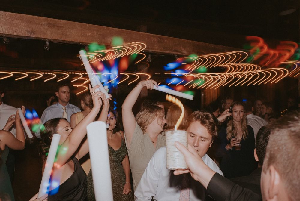 Guests dancing with glow sticks at a lively wedding reception party under colorful light trails.