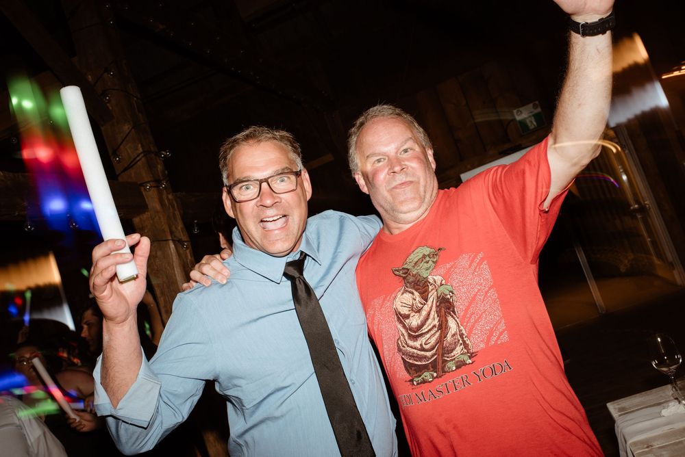Two men smiling and celebrating at a party, one holding a glow stick and wearing a Yoda t-shirt.