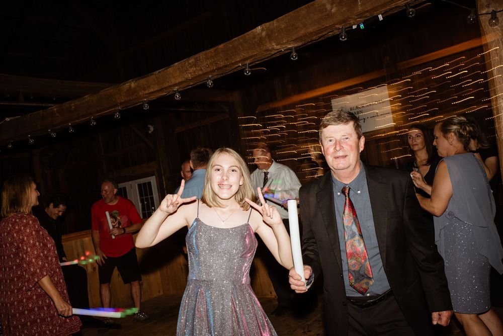 Two people smile and dance together at an indoor party event with other guests in the background.