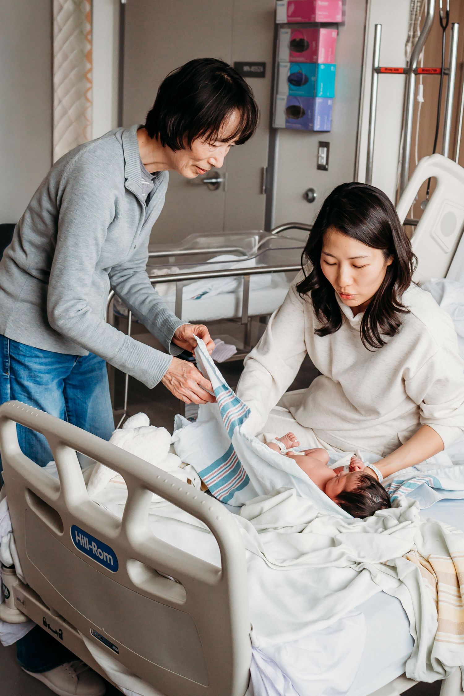 New parents admiring their newborn baby in a hospital room, mother resting in bed while father leans in closely.