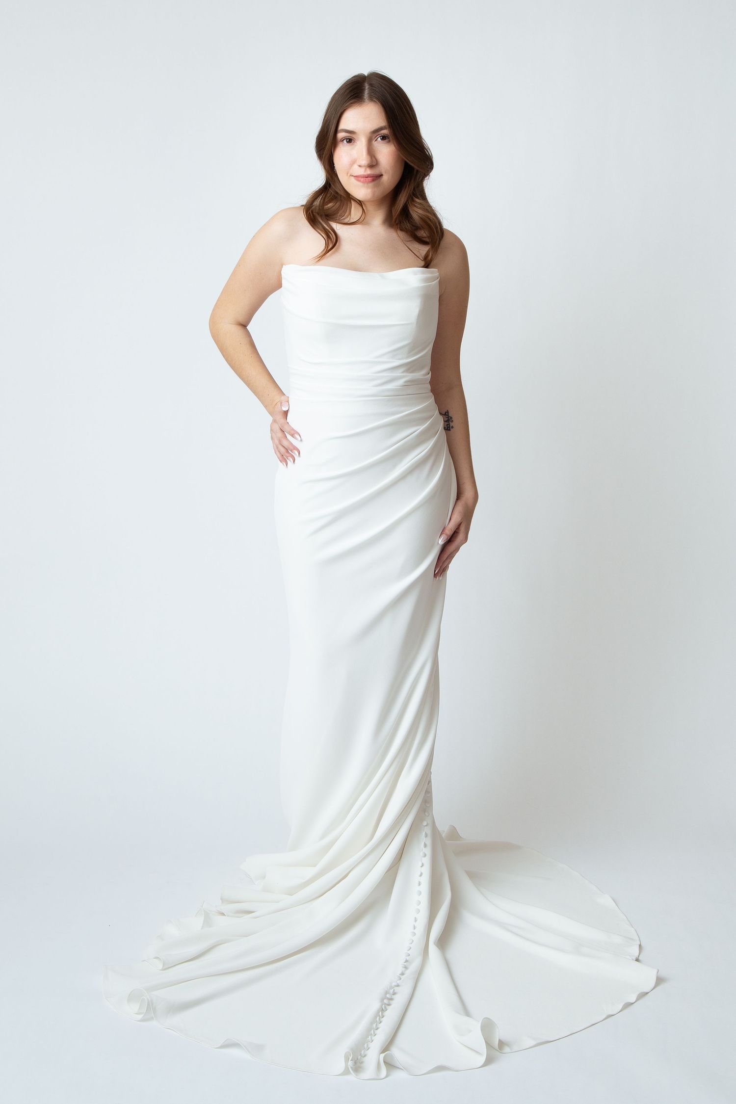 Full length photo of a bride in a form fitting wedding gown with a train against a white background at Celebrations Bridal and Prom NBTX