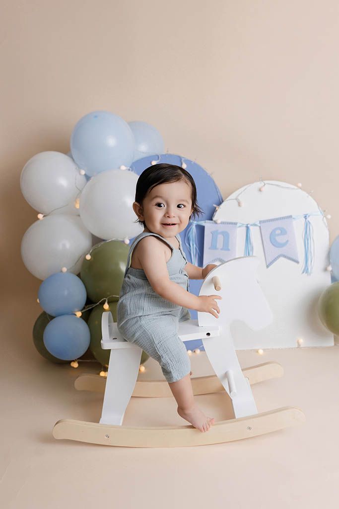 Affordable Menifee photographer photo of baby boy  on white rocking horse surrounded by balloons for his first birthday.