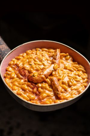 A skillet of creamy mac and cheese topped with grilled sausage slices and a sprinkle of paprika.