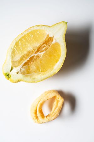 A halved squeezed lemon with a small piece of lemon rind on a white background.