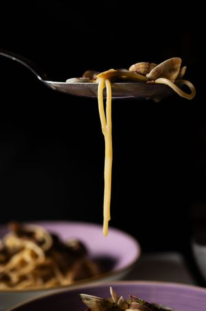 Spaghetti alle vongole being lifted on a spoon with clams, noodles draping down over a purple plate.