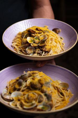 Two purple bowls of spaghetti alle vongole with clams held by a person.