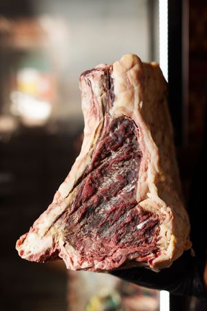 Close-up of a large dry-aged beef cut showing deep red marbling and fat cap on dark background.