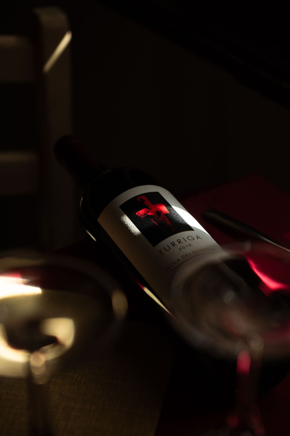 Turrida red wine bottle with glass in moody dark restaurant lighting.