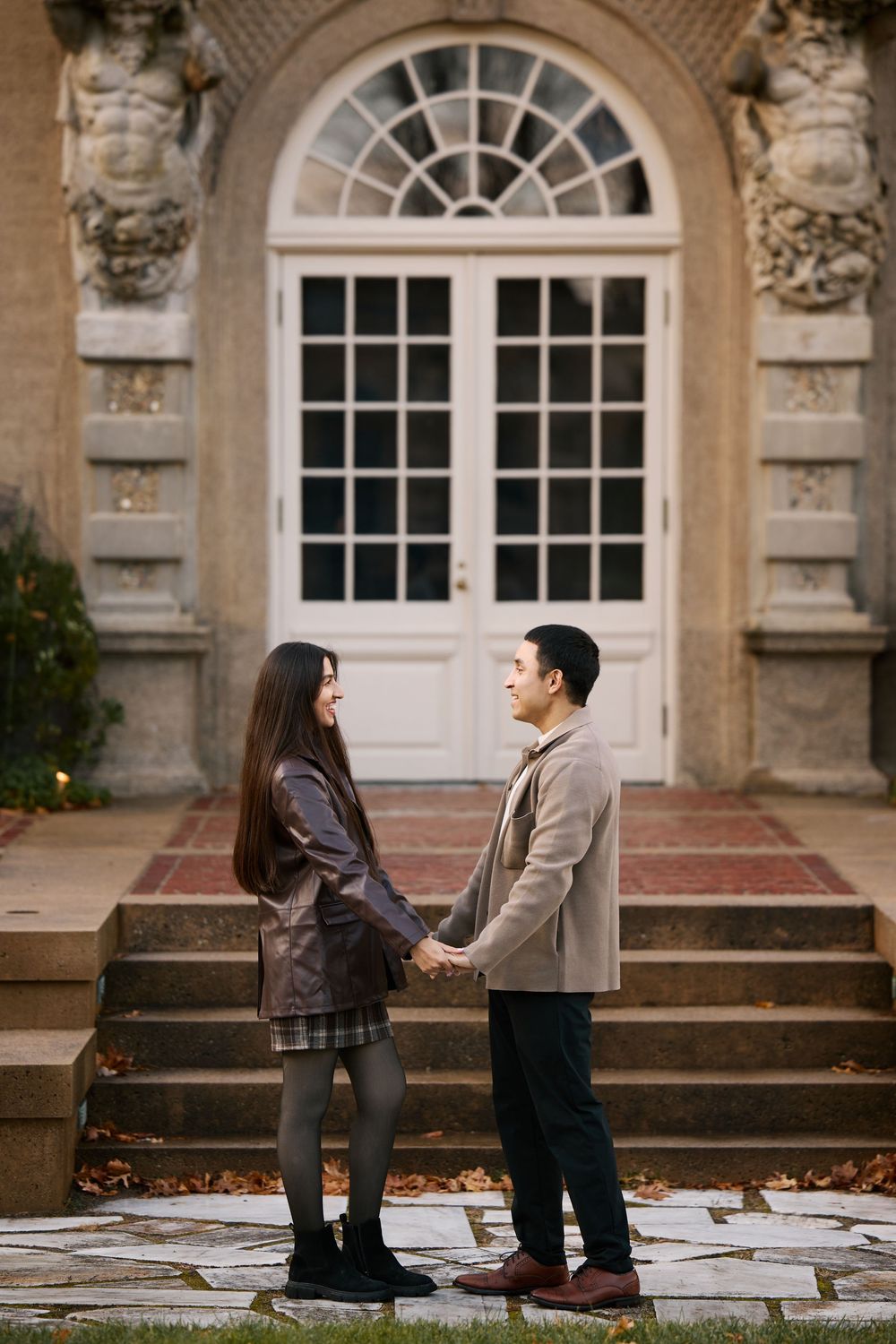 Couple holding hands facing each other before elegant arched doorway.
