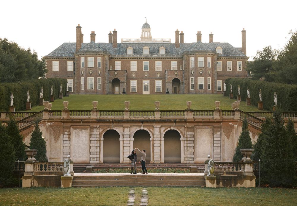 Couple walking toward grand historic brick mansion with terraced gardens.