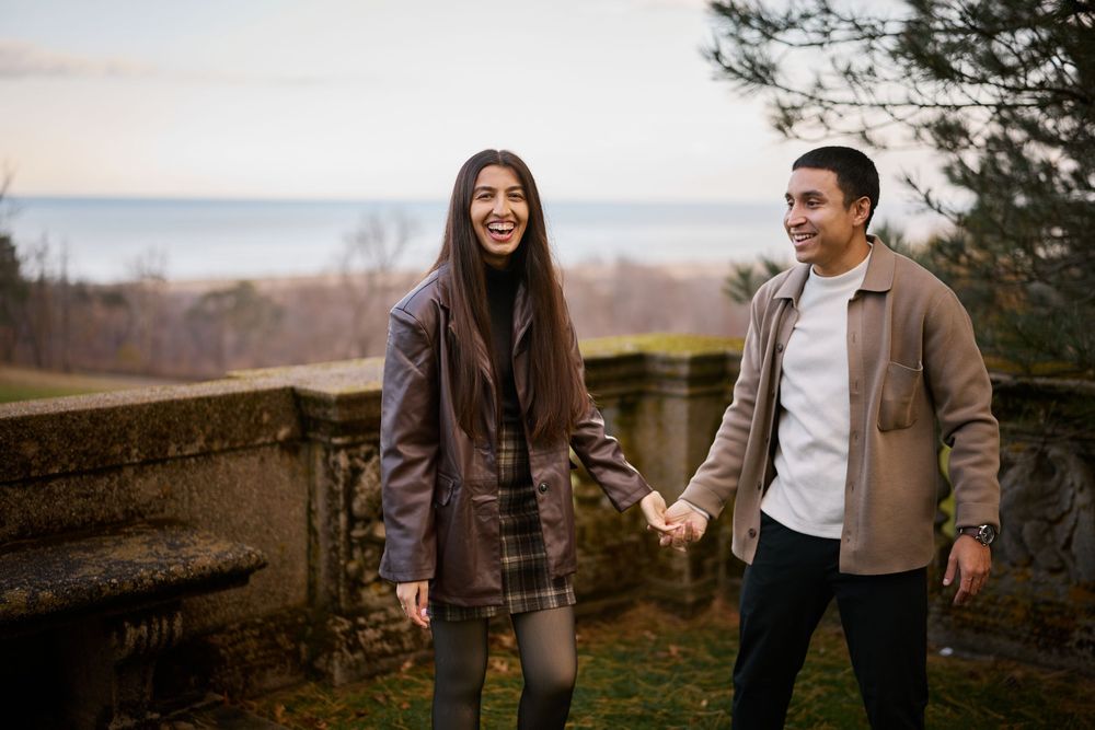 Joyful couple holding hands walking along stone balustrade with ocean view.