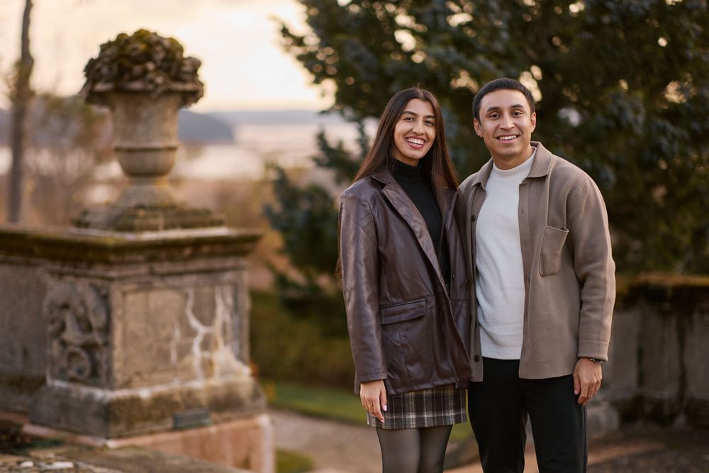 Smiling couple posing together outdoors near stone urns at golden hour.