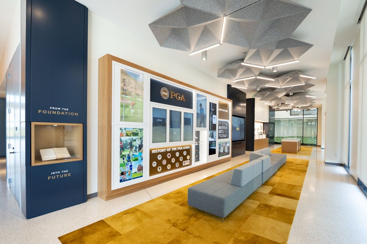 Modern corporate lobby with blue display wall, PGA branding, gold carpet, and geometric ceiling panels.