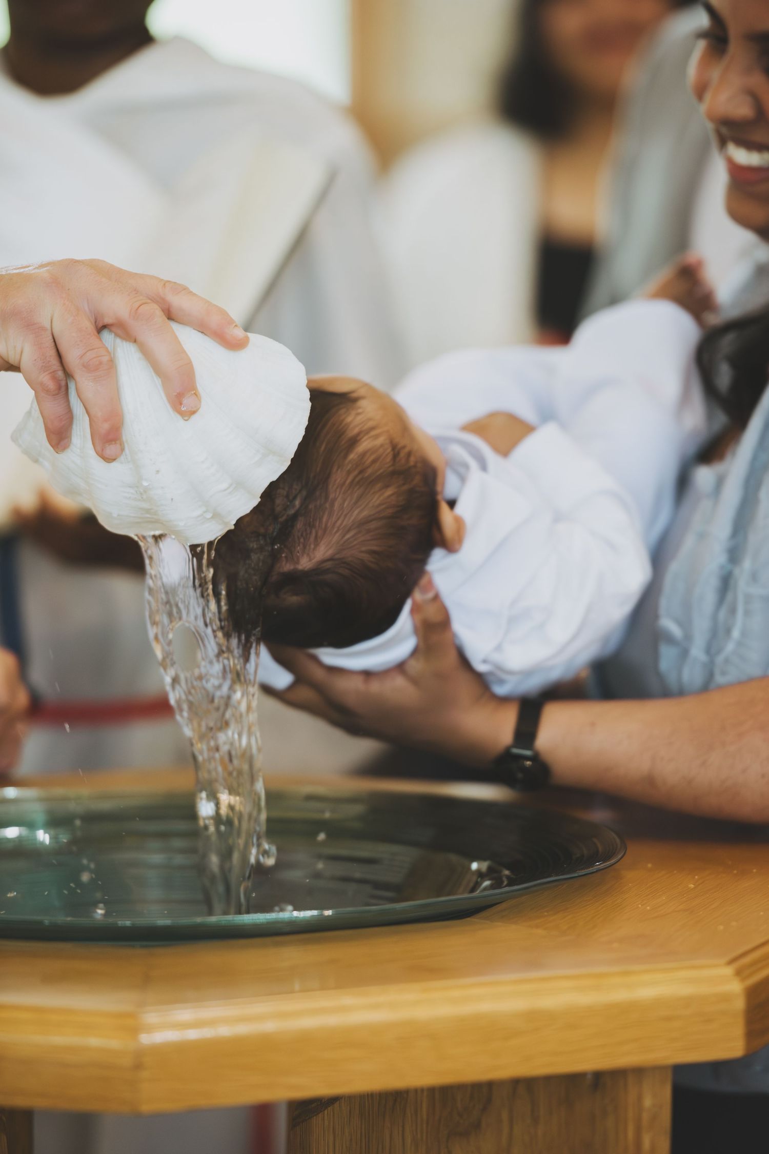 A baby being baptized with water poured over its head at a church font during a christening ceremony.