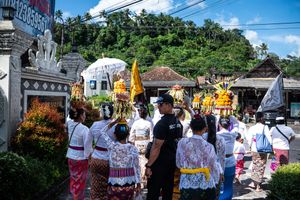 Colorful Balinese Hindu procession with locals in traditional attire carrying ceremonial offerings through a village street.