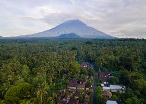Aerial view of a lush tropical forest village with a majestic volcanic mountain rising in the misty background.