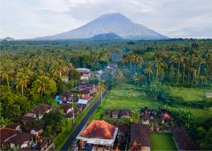 Aerial view of a lush tropical village with palm trees and a majestic volcano in the background in Bali, Indonesia.