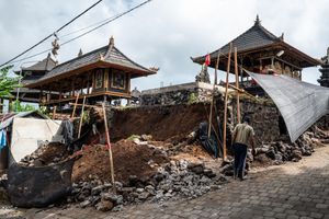 Construction workers restoring traditional Balinese temple structures with bamboo scaffolding and excavated earth on site.