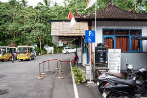 Parking area with motorcycles, blue disability sign, Indonesian flag, yellow buses, and lush green trees in Bali, Indonesia.