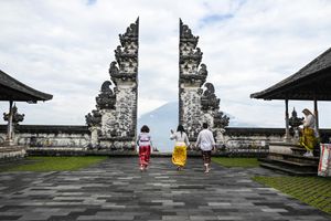 Two visitors walk through the iconic split gate of Pura Lempuyang temple in Bali with a volcano backdrop.