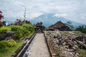 Stone pathway leading to a Balinese temple with a misty volcano and tropical gardens in background.