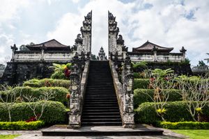 Ancient Balinese Hindu temple gate with ornate stone carvings, symmetrical split gateway and lush tropical gardens in Bali.