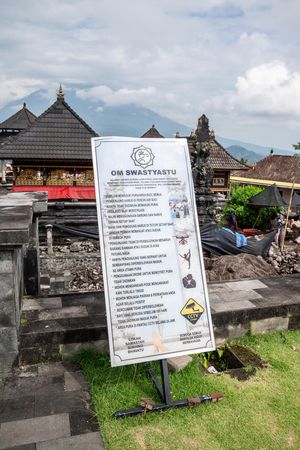 Om Swastyastu sign at Balinese Hindu temple with traditional architecture and mountain backdrop in Bali, Indonesia.