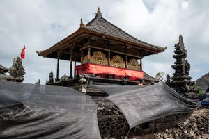 Balinese temple with ornate golden pavilion covered by black protective tarp during restoration work under cloudy sky.