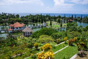 Aerial view of Taman Ujung water palace in Bali with tropical gardens, ponds, and ocean backdrop.