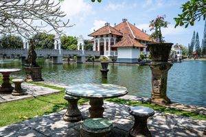Balinese water palace with ornate stone tables, lush gardens, and a serene pond reflecting traditional architecture.