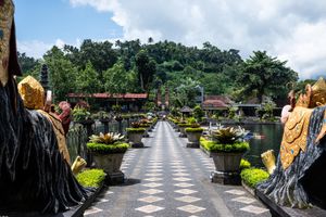 Scenic pathway lined with golden statues and tropical plants leading to a Balinese temple complex.