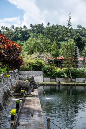 Serene Balinese water palace pool with stone dragon fountains, lush tropical gardens, and tiered pagoda backdrop.