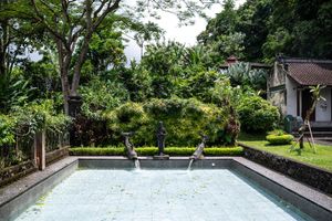 Tranquil garden pool with stone statues, lush tropical greenery, and traditional Balinese architecture in a serene outdoor setting.