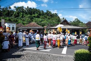 Balinese Hindu procession with people in traditional white and colorful attire walking through a village street.