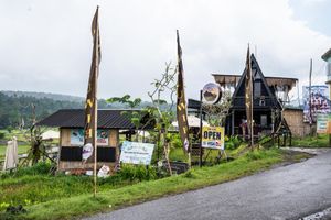A rustic roadside shop with an A-frame building and open sign surrounded by lush greenery on a cloudy day.