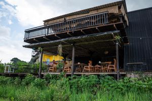 Rustic two-story wooden restaurant with outdoor dining terrace surrounded by lush green vegetation.