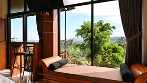 Luxury hotel room with floor-to-ceiling windows offering panoramic tropical garden and hillside views with a cozy window seat.