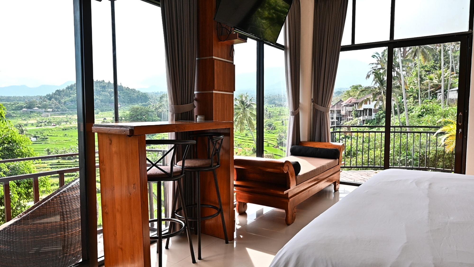 Elegant hotel room featuring large windows with lush green valley views, wooden furniture, and a classic daybed sofa.