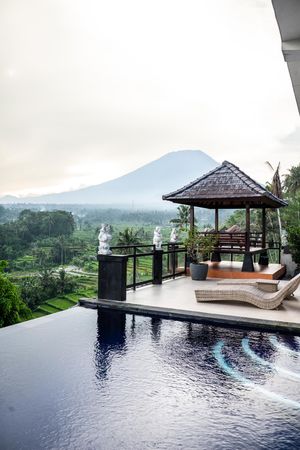 Luxury infinity pool overlooking lush Bali rice terraces with gazebo and mountain view at resort.