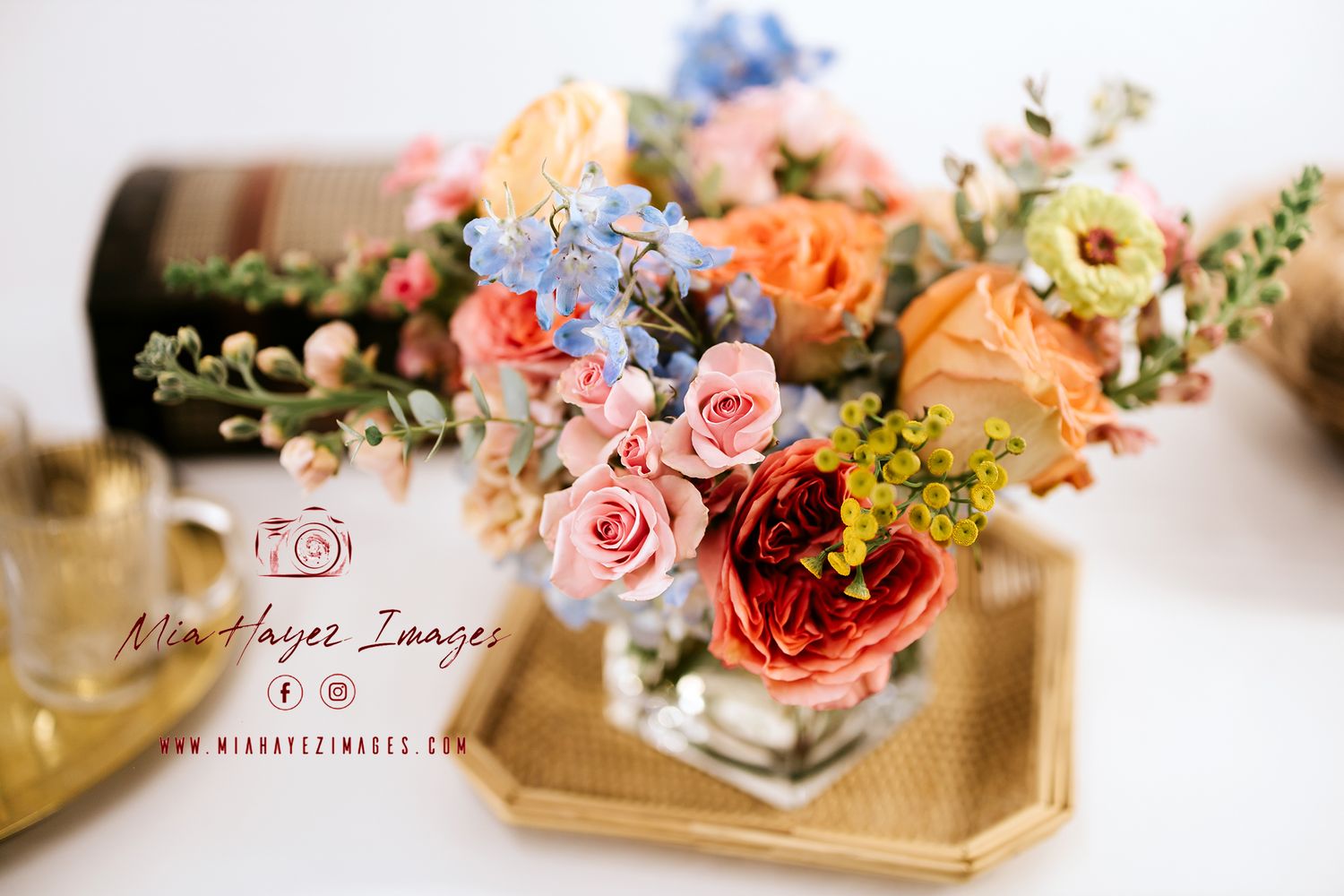 Colorful floral arrangement with pink, red, orange, and blue flowers in a glass vase on a golden tray.