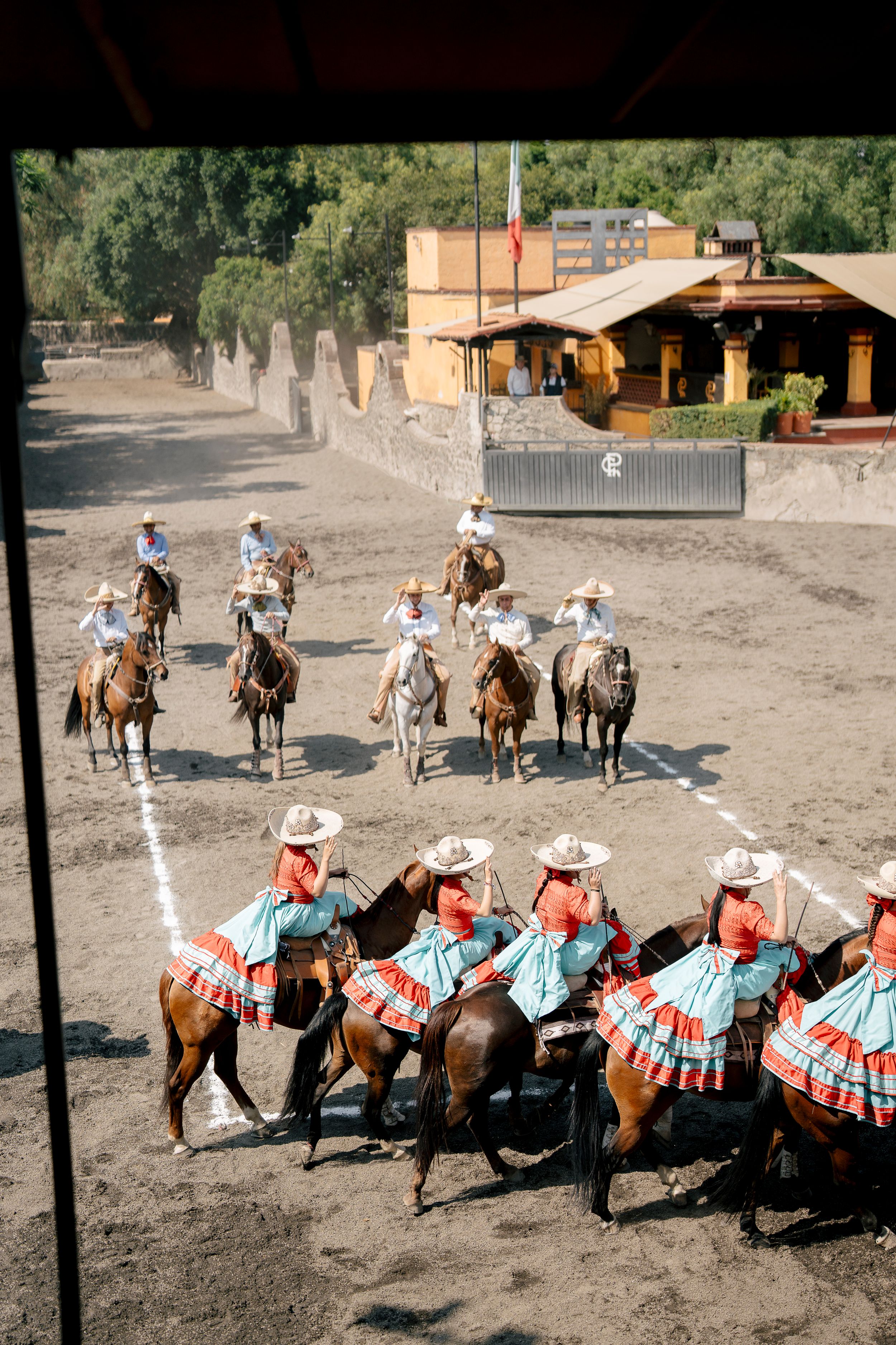 Black and white photo of Mexican charras in sombreros riding horses in a row at a traditional charrería event.